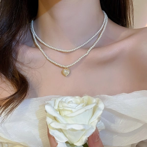 Close-up of double-layer pearl necklace with heart pendant and soft white rose background