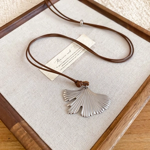 Detail of silver ginkgo leaf pendant on brown cord over a rustic linen surface