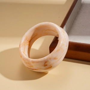 Close-up of wide resin bangle with marble texture and amber accents on minimalist wood background