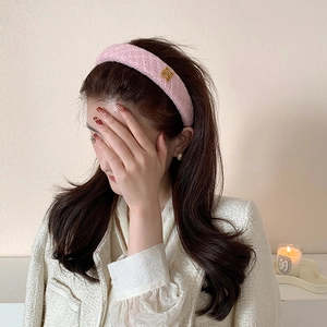Dettaglio di un cerchietto imbottito in tweed rosa con logo in metallo dorato