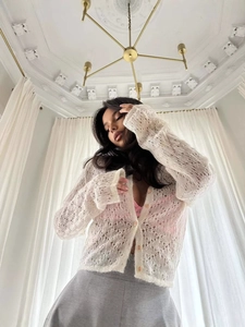 White hollow-out knit cardigan with long sleeves and delicate texture in low angle view