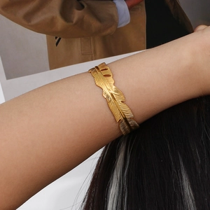 Detailed close-up of a 18K gold-plated stainless steel feather cuff bracelet on a wrist