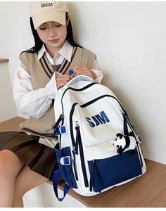 Detail of college style cream backpack with blue SJM print and cute panda charm