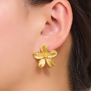 Golden five-petal flower stud earrings with brushed metal texture worn on ear