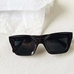 Detailed close-up of glossy black square sunglasses frames on textured background