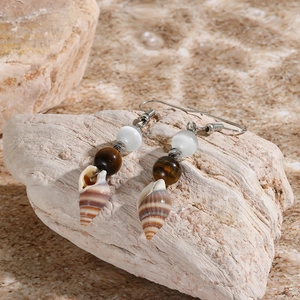 Detailed close-up of shell and tiger eye stone earrings on a natural rock surface