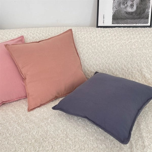 Close-up of pink and orange square pillowcases on a white sofa with neat stitched edges