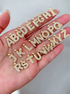 Detailed view of 26 golden alphabet pendants with inlaid rhinestones held in hand