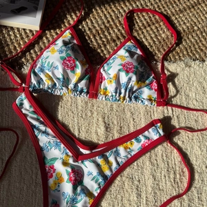 Flat lay of floral bikini with red straps on straw mat under bright summer sunlight