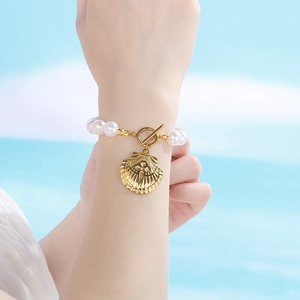 Macro detail of white pearl bracelet featuring a golden seashell charm and OT toggle clasp