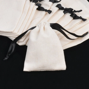 Detailed close-up of beige cotton jewelry drawstring bags with elegant black ribbon bows