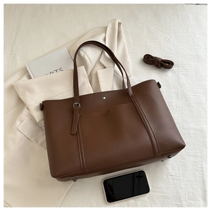 Flat lay of brown tote bag with shoulder strap, small book, and beige blazer on white fabric