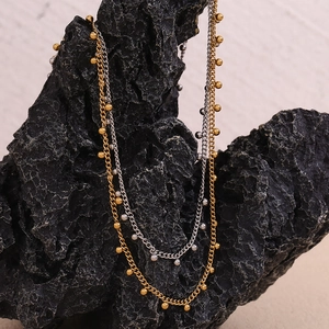 Detail of double-layer stainless steel necklace with gold and silver beads on volcanic rock