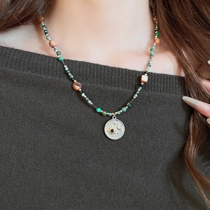 Détail d'un collier de perles avec pendentif céleste sur un pull en maille sombre