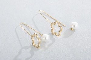 Close-up of golden clover earrings with shimmering diamonds and white pearl drops