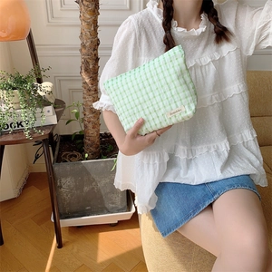 Portable green and white checkered makeup bag with woven label in a lifestyle setting