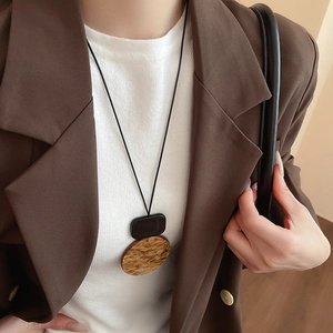 Detail of a geometric resin pendant with faux wood texture on a black cord necklace