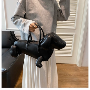 Close-up of a designer black leather dachshund dog shaped handbag held by a model