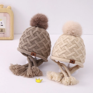 Detail of knit baby earflap hats with braided tassels and fluffy faux fur pom-poms