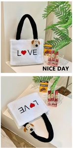 Detail of white plush tote bag with black handles and embroidered LOVE logo