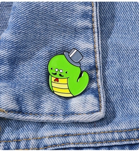 Close-up of a cartoon green snake enamel pin with a top hat on blue denim fabric