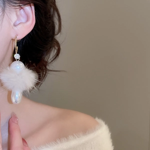 Detail of model wearing C-shaped earrings with soft white fur balls and teardrop pearls