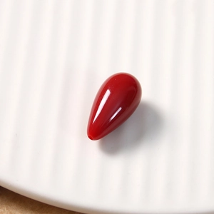 Detailed view of a red teardrop resin bead with top-drilled hole on a white tray