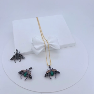 Detailed view of bug-themed necklaces with green and brown gemstones in a white gift box