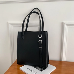 Minimalist black leather tote bag with silver ring and strap details on a desk