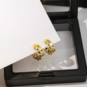 Vue détaillée de boucles d'oreilles dorées avec texture chaîne sur un écrin noir
