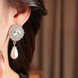 Close-up of a silver earring with a square rhinestone and a teardrop pearl on a model