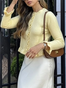 Detail of yellow knit cardigan featuring scalloped edges and buttons in outdoor light
