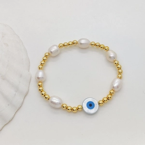 Baroque pearl bracelet with gold beads and blue evil eye charm on white shell background