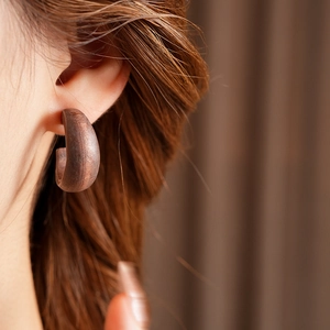 Close-up of vintage dark brown wooden C-shaped earrings with natural grain on a model