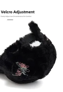 Close-up of black plush hat showing adjustable hook and loop strap and floral embroidery