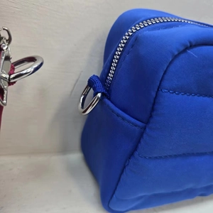 Detail of blue quilted nylon crossbody bag showing the metal D-ring and smooth zipper
