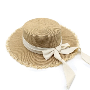 Summer raffia sun hat with flat top, beige ribbon bow and fringe brim for beach