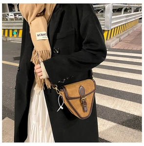 Foto callejera de un bolso de silla de montar en cuero mate con hebilla y bufanda beige