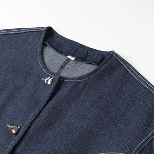 Détail d'un haut en jean bleu foncé avec col rond et boutons métalliques dorés