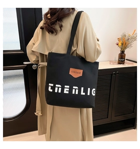 Detail of a large black canvas tote bag with white lettering and brown leather logo patch