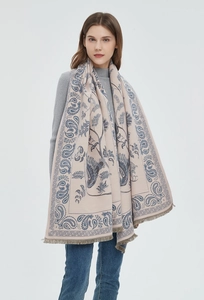 Detail of beige scarf with blue paisley pattern and fringe trim on a female model