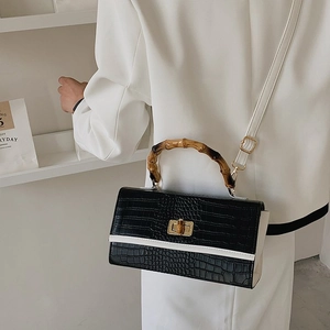Black crocodile pattern handbag with bamboo handle and gold lock detail shown on a model
