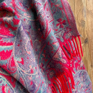 Detailed close-up of ethnic paisley knit shawl with vibrant red tassels on wood texture