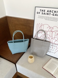 Detailed view of handmade woven straw tote bags in light blue and grey on a wooden bench