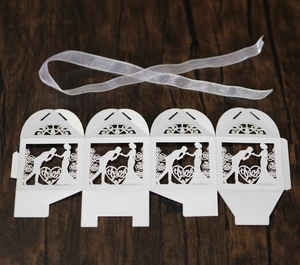 Detailed laser-cut wedding candy box with heart motifs and silk ribbon on wood surface