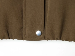 Detail view of brown woven bomber jacket hem featuring a polished silver metal snap button