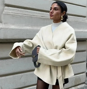 Manteau en laine crème avec ceinture à la taille et coupe drapée lors d'un shooting rue