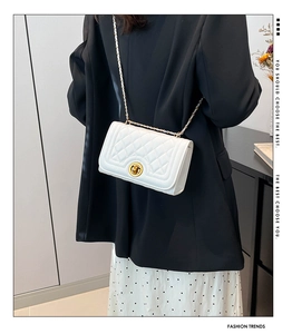 Detail of white quilted chain bag with gold metal lock and leather strap crossbody