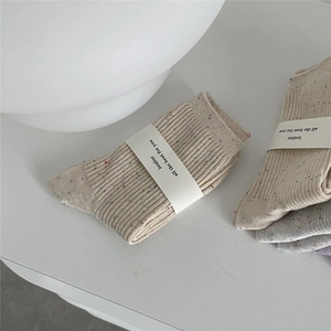 Close-up of ribbed cotton socks in off-white with colorful confetti dots and paper wrap