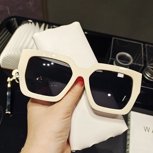 Detailed view of oversized square cream sunglasses with dark lenses and leather case